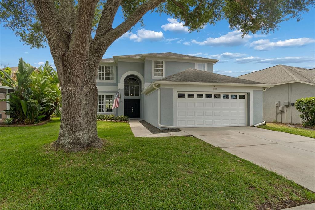 A two-story house with a gray stucco exterior, a large tree, and a two-car garage — 1324 BROOKE VIEW DRIVE, ODESSA, FL