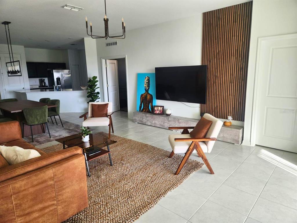 A living room features a wall-mounted television, wood slat accent wall, and tiled flooring — 4615 WANDSWORTH WAY, DAVENPORT, FL