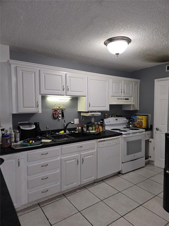 A kitchen features white cabinets, dark countertops, a white stove, and tiled flooring — 6400 46TH AVENUE N UNIT 305, KENNETH CITY, FL
