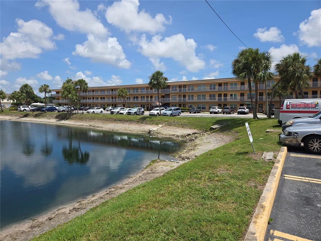 A multi-story apartment building sits behind a parking lot and a small pond — 6400 46TH AVENUE N UNIT 305, KENNETH CITY, FL