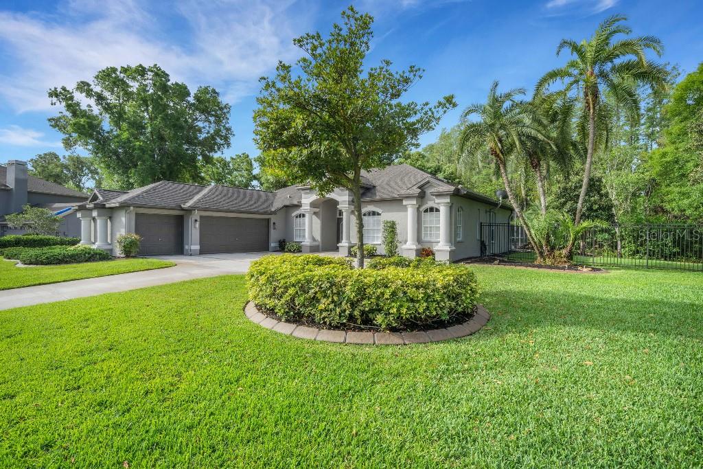 A single-story house with a three-car garage, a circular garden bed, and palm trees — 18212 KEYSTONE GROVE BOULEVARD, ODESSA, FL