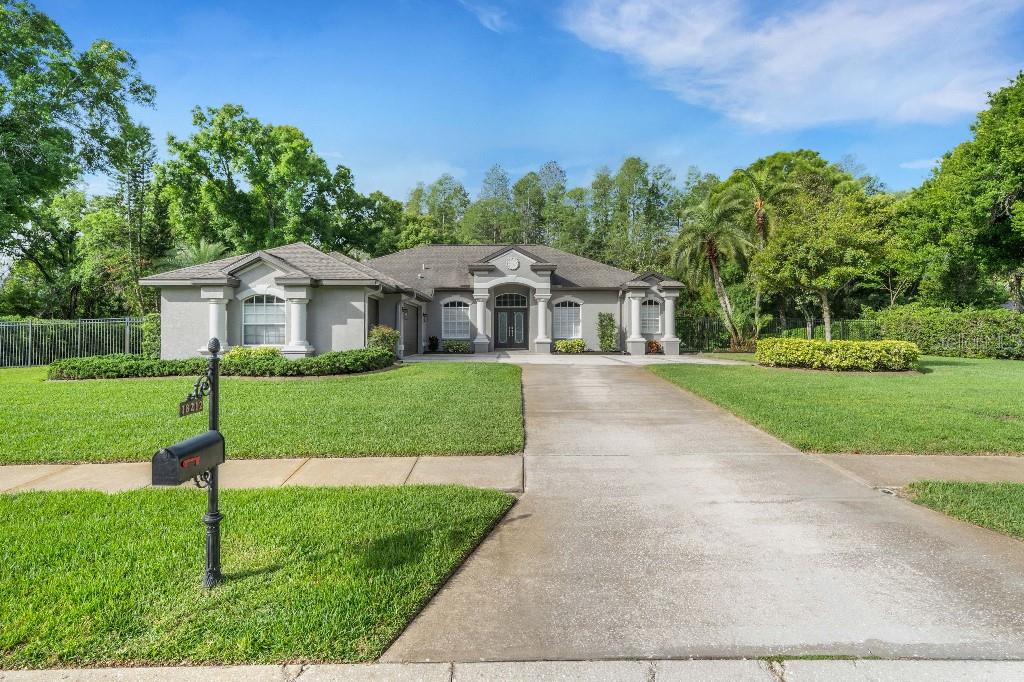 A single-story house with a gray stucco exterior, a concrete driveway, and a manicured lawn — 18212 KEYSTONE GROVE BOULEVARD, ODESSA, FL