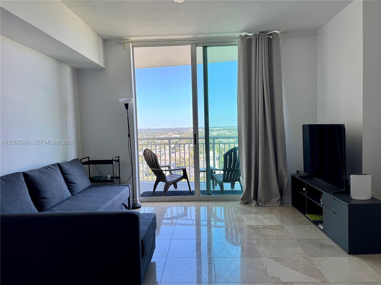 A living room features a dark sofa, a television console, and a balcony with outdoor chairs — 1745 E Hallandale Beach Blvd # 2001W, Hallandale Beach FL 33009, HALLANDALE BEACH, FL