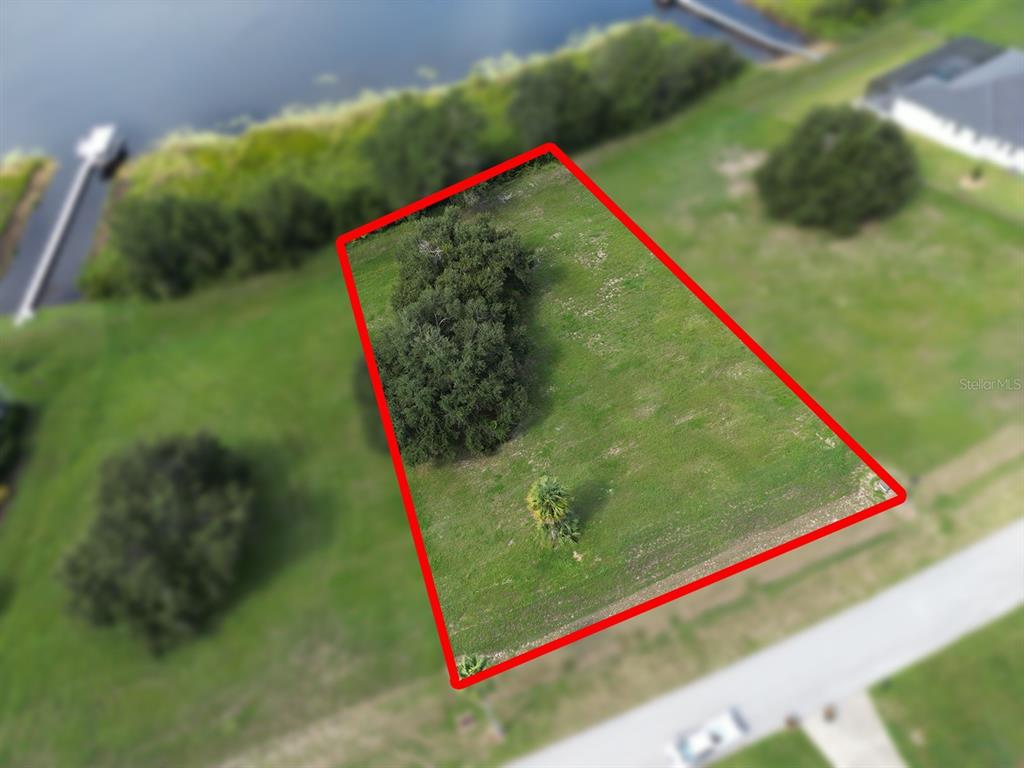 An aerial view shows a vacant, grassy lot outlined in red near a body of water — ROYAL PALM DRIVE UNIT 15, GROVELAND, FL