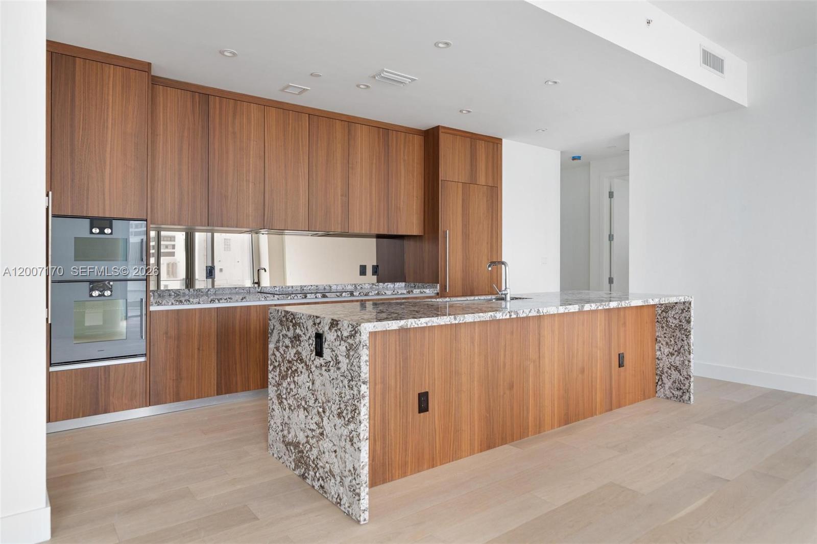 A modern kitchen features wood cabinetry, granite countertops, a waterfall island, and stainless steel appliances — 175 SE 25th RD # 1904, Miami FL 33129, MIAMI, FL