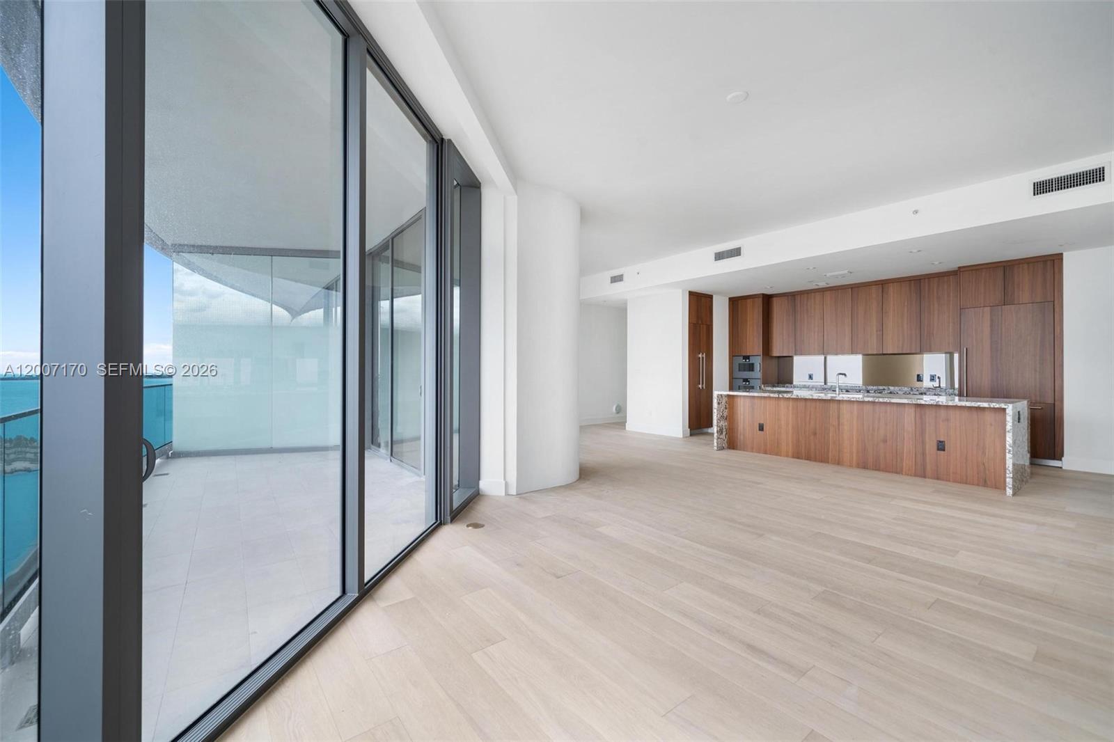 A modern kitchen with wood cabinetry and a stone island overlooks a spacious balcony — 175 SE 25th RD # 1904, Miami FL 33129, MIAMI, FL