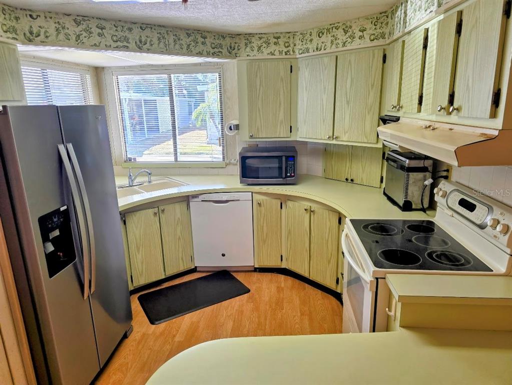 A kitchen with light wood cabinets, stainless steel appliances, and a curved countertop layout — 12501 ULMERTON ROAD UNIT 188, LARGO, FL