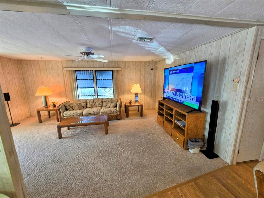 A living room features wood-paneled walls, beige carpeting, a floral sofa, and a television console — 12501 ULMERTON ROAD UNIT 188, LARGO, FL