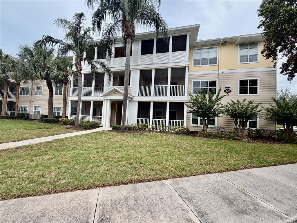 A three-story apartment building with screened balconies and beige siding sits behind a grassy lawn — 4802 51ST STREET W UNIT 409, BRADENTON, FL
