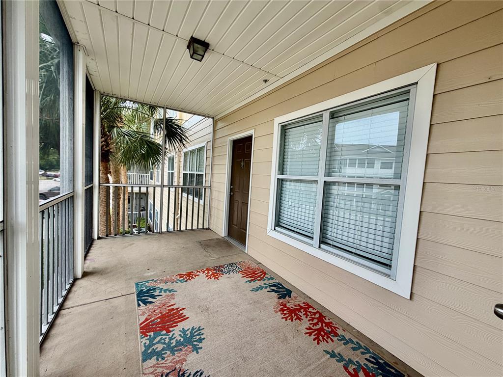 A screened-in balcony with a concrete floor, a patterned rug, and a brown entry door — 4802 51ST STREET W UNIT 409, BRADENTON, FL