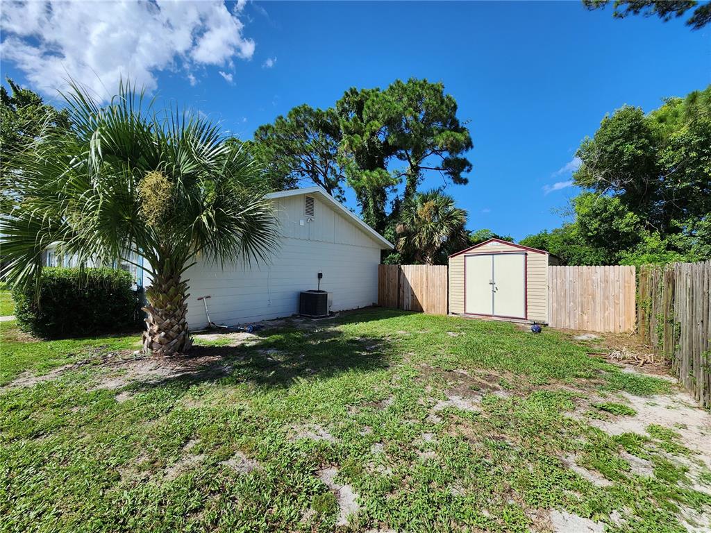 A backyard features a palm tree, a beige house exterior, a storage shed, and wooden fencing — 1917 FERN PALM DRIVE, EDGEWATER, FL