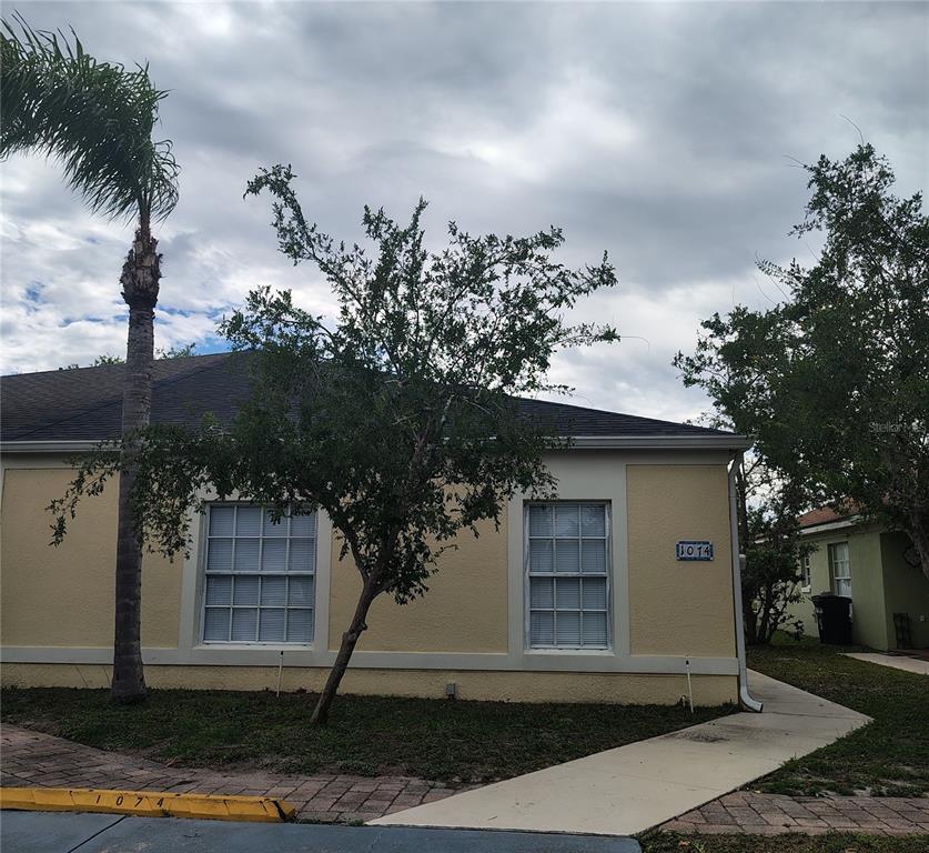 A single-story tan house with a palm tree, a small tree, and a concrete walkway — 1074 UNIVERSAL REST PLACE, KISSIMMEE, FL