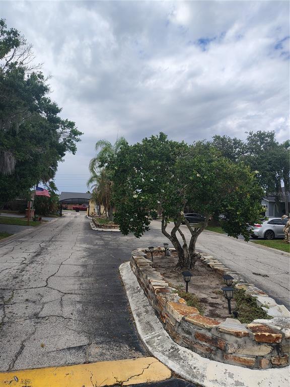 A paved driveway leads toward a gated entrance with a stone-walled tree planter in front — 1074 UNIVERSAL REST PLACE, KISSIMMEE, FL