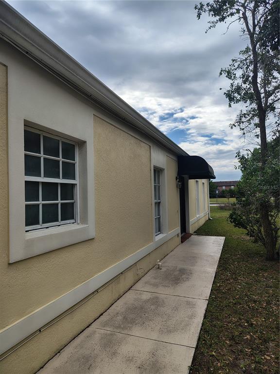 A side view of a yellow stucco building with a concrete walkway and black awning — 1074 UNIVERSAL REST PLACE, KISSIMMEE, FL