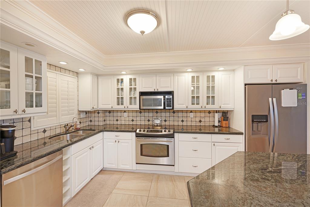 A white kitchen features dark granite countertops, stainless steel appliances, and a beadboard ceiling — 5600 BEACH WAY DR UNIT 213, SARASOTA, FL