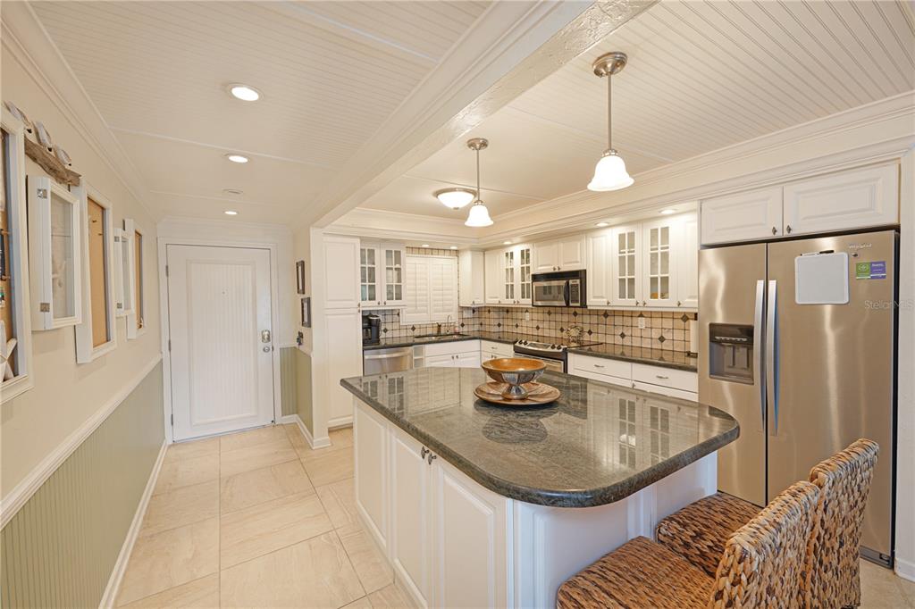 A kitchen features white cabinetry, a dark granite island, stainless steel appliances, and tile flooring — 5600 BEACH WAY DR UNIT 213, SARASOTA, FL