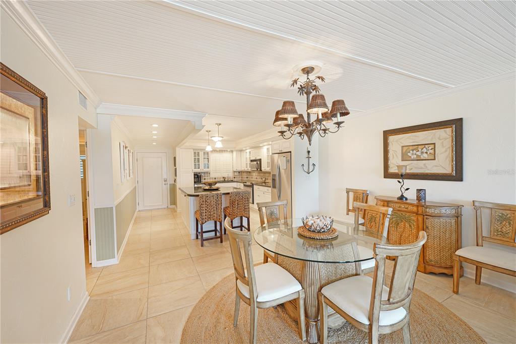 A dining area with a glass table and chandelier opens into a kitchen with island seating — 5600 BEACH WAY DR UNIT 213, SARASOTA, FL