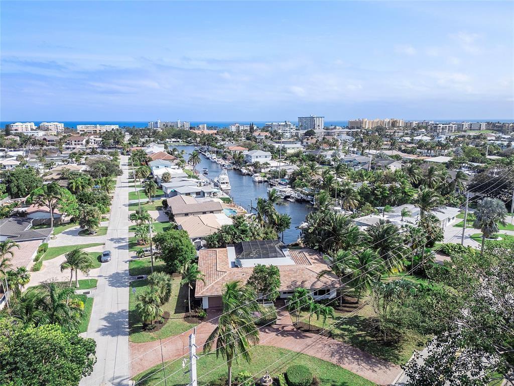 An aerial view shows a residential neighborhood with a canal, palm trees, and coastal buildings — 556 SE 15th Avenue, Deerfield Beach FL 33441, DEERFIELD BEACH, FL