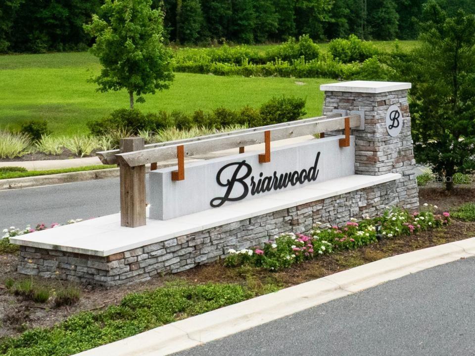 A stone and wood monument sign for Briarwood stands beside a paved road and lawn — 16780 NW 16780 NW 178TH TER, ALACHUA, FL