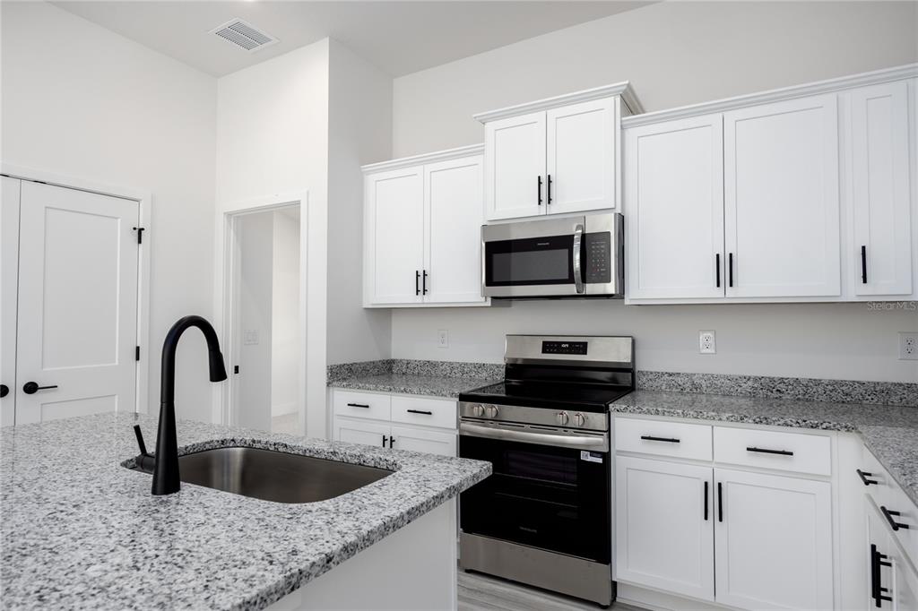 A kitchen features white cabinets, granite countertops, stainless steel appliances, and a black faucet — 16780 NW 16780 NW 178TH TER, ALACHUA, FL