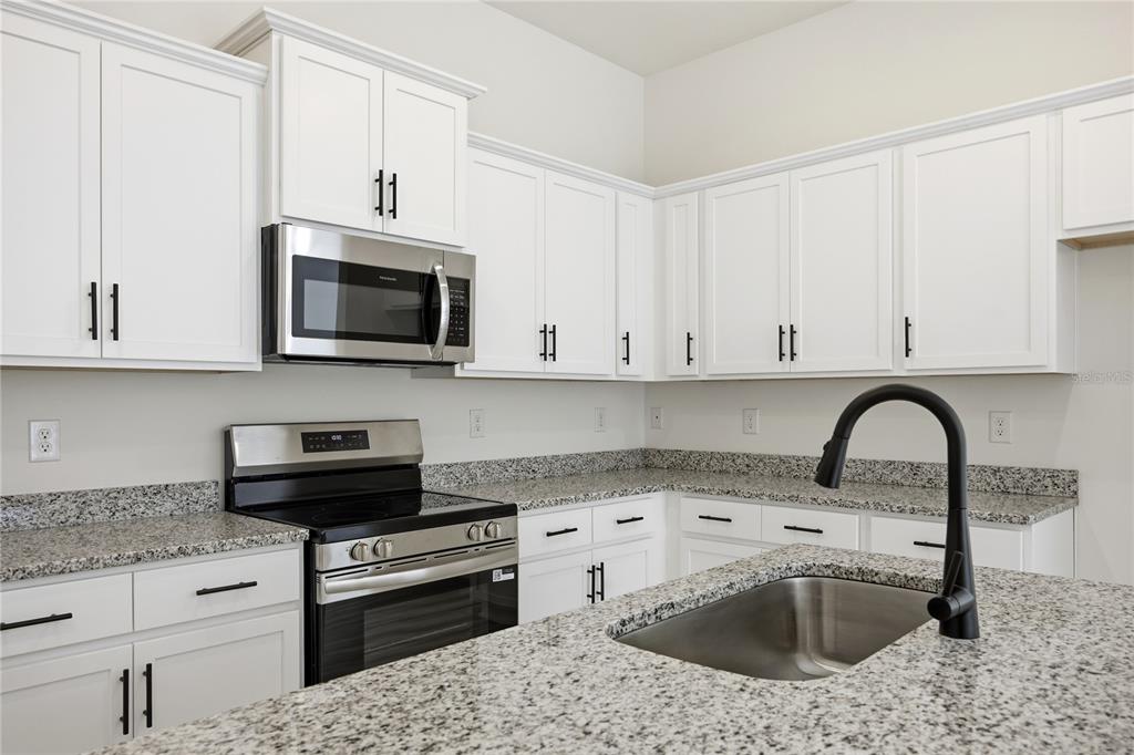 A kitchen features white cabinets, granite countertops, stainless steel appliances, and a black faucet — 16780 NW 16780 NW 178TH TER, ALACHUA, FL