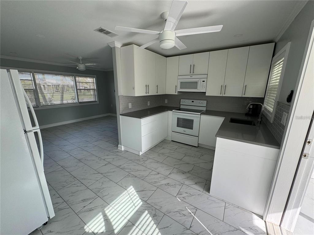 A kitchen with white cabinets, gray countertops, and white marble-patterned tile flooring — 301 COLONIA LANE W, NOKOMIS, FL