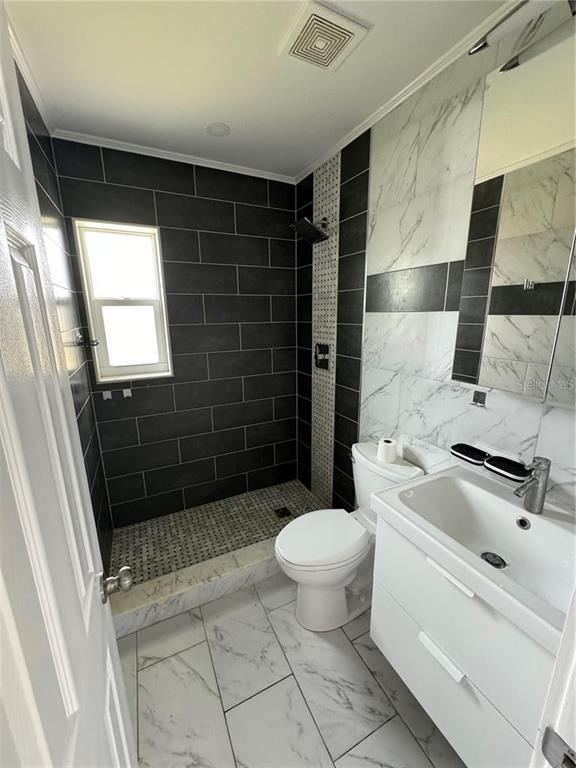 A bathroom features a walk-in shower with dark tiles, a white vanity, and marble-patterned flooring — 301 COLONIA LANE W, NOKOMIS, FL