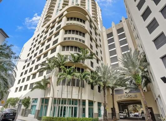 A low-angle view of a tall, beige apartment building with palm trees in front — 9066 SW 73rd Ct # 1703, Miami FL 33156, MIAMI, FL