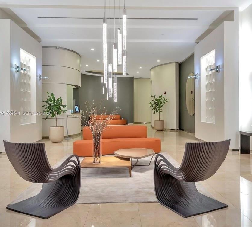A modern lobby features two sculptural dark chairs, orange sofas, and a tiered pendant light — 9066 SW 73rd Ct # 1703, Miami FL 33156, MIAMI, FL