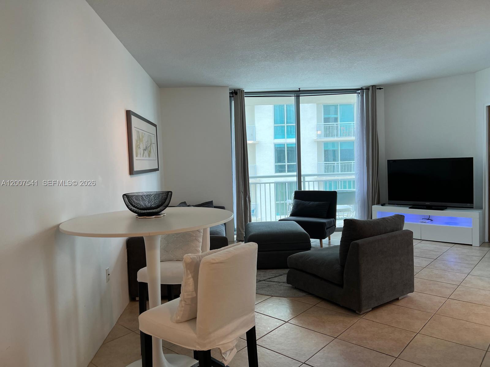 A living and dining area features tile floors, a white table, and a balcony view — 9066 SW 73rd Ct # 1703, Miami FL 33156, MIAMI, FL