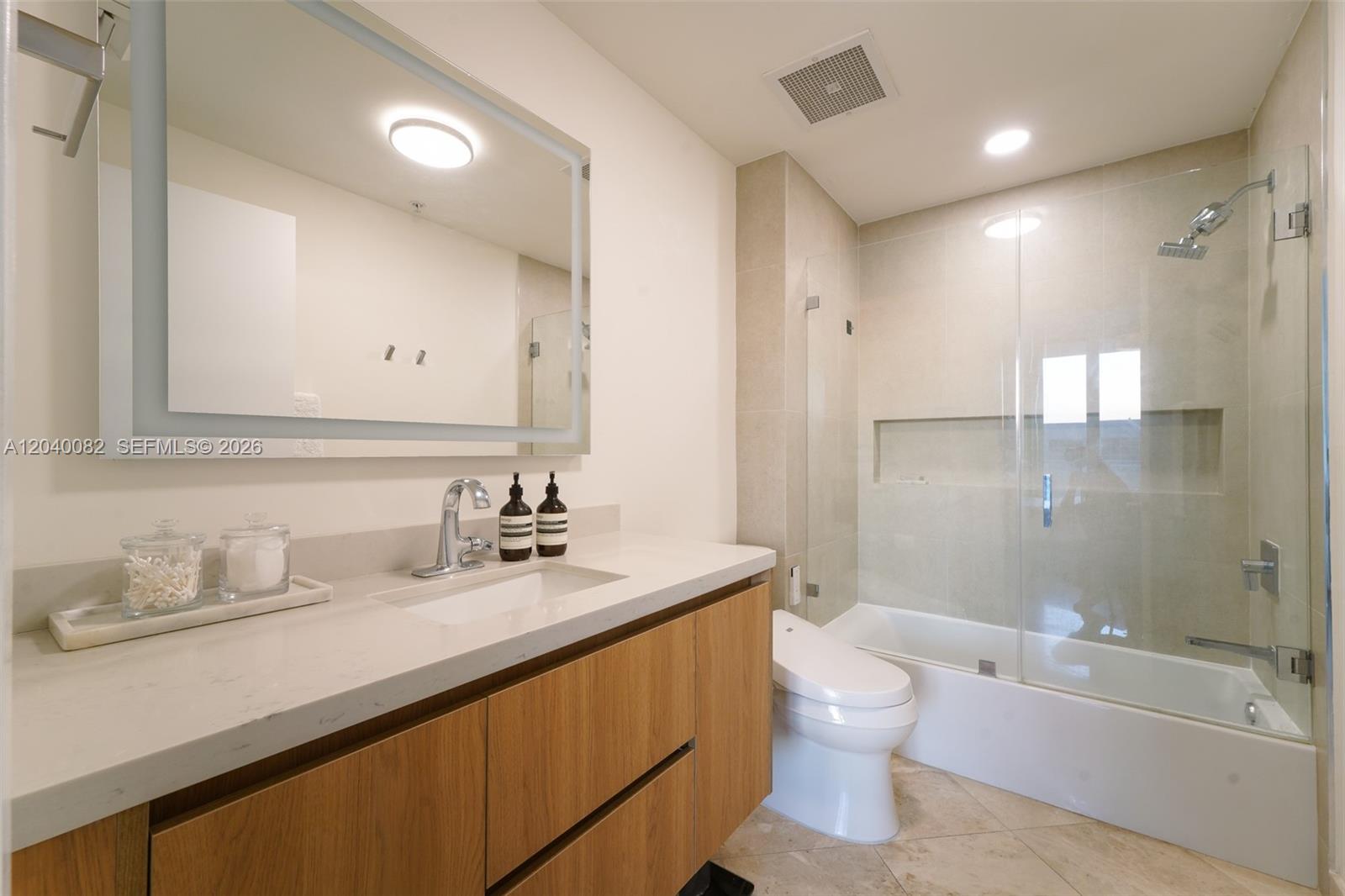 A modern bathroom features a wood vanity, a glass-enclosed shower-tub combo, and a lighted mirror — 3470 E Coast Ave # H1109, Miami FL 33137, MIAMI, FL