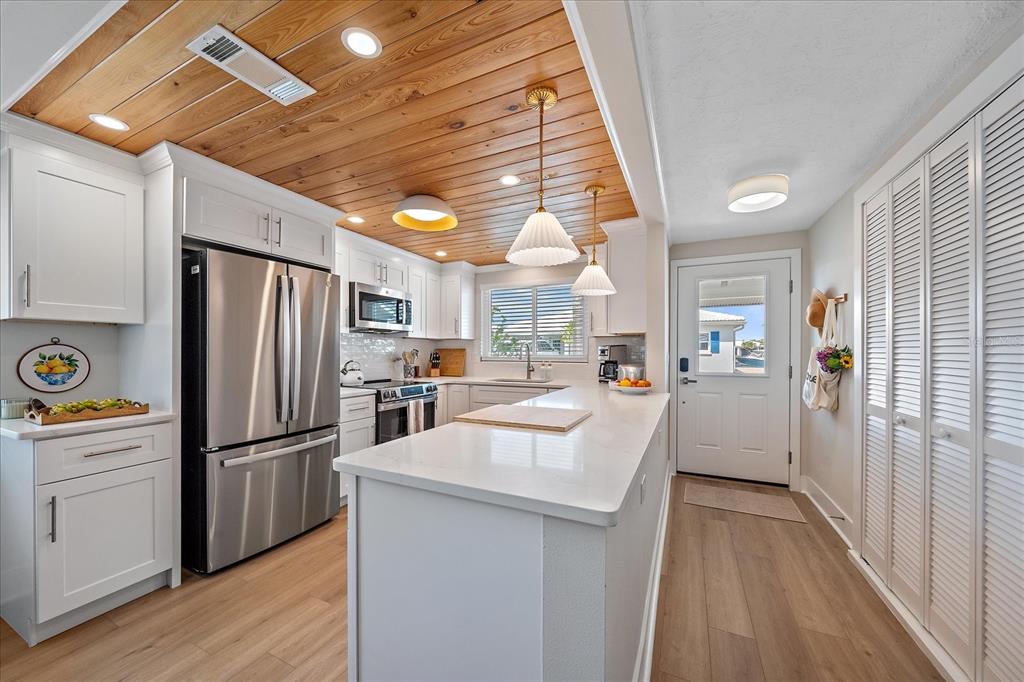 A kitchen features white cabinets, stainless steel appliances, a quartz island, and a wood-plank ceiling — 914 SPANISH DRIVE S UNIT 76, LONGBOAT KEY, FL