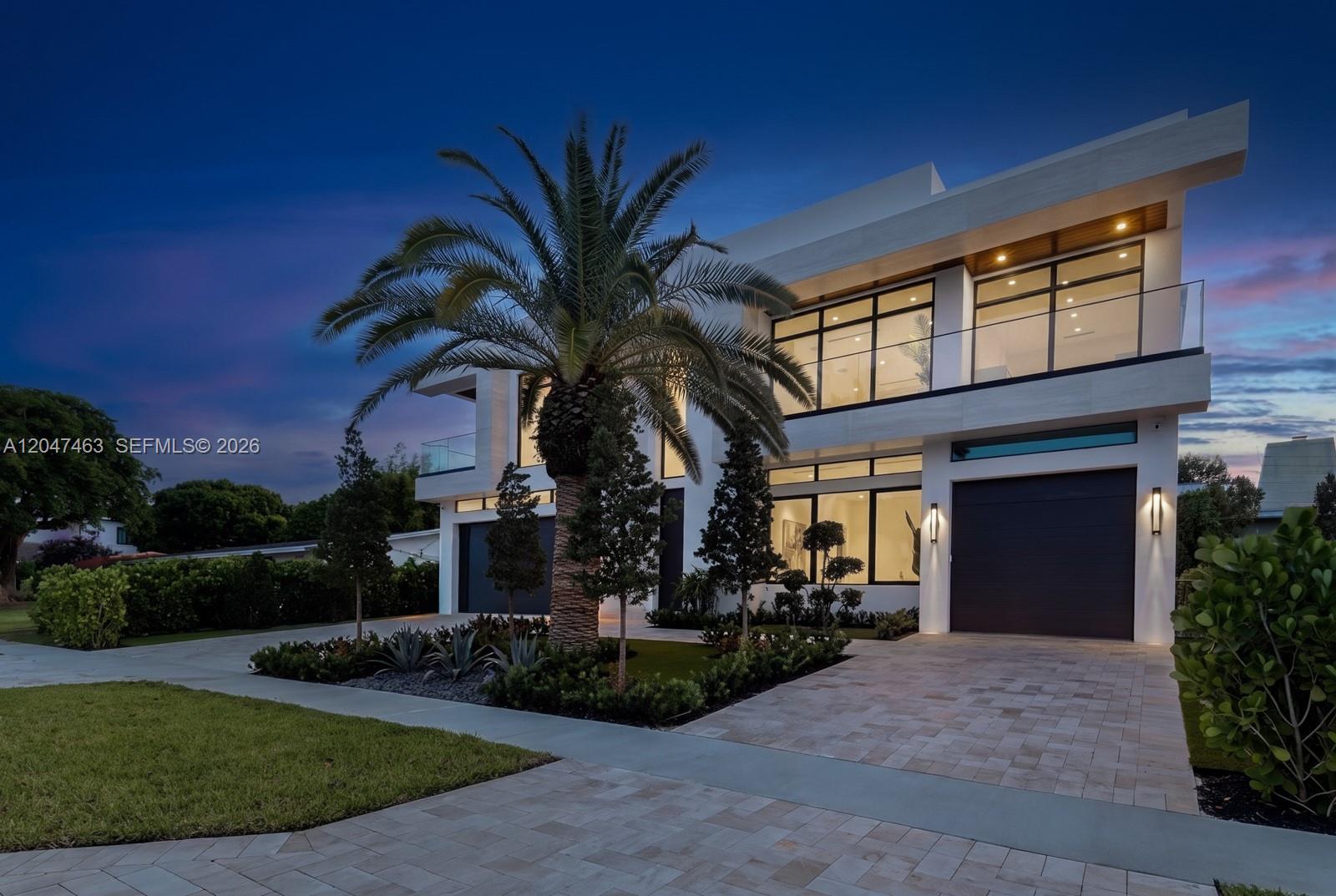 A modern two-story house with a palm tree, paved driveway, and glass balcony at dusk — 1051 NE 2nd Ter, Boca Raton FL 33432, BOCA RATON, FL