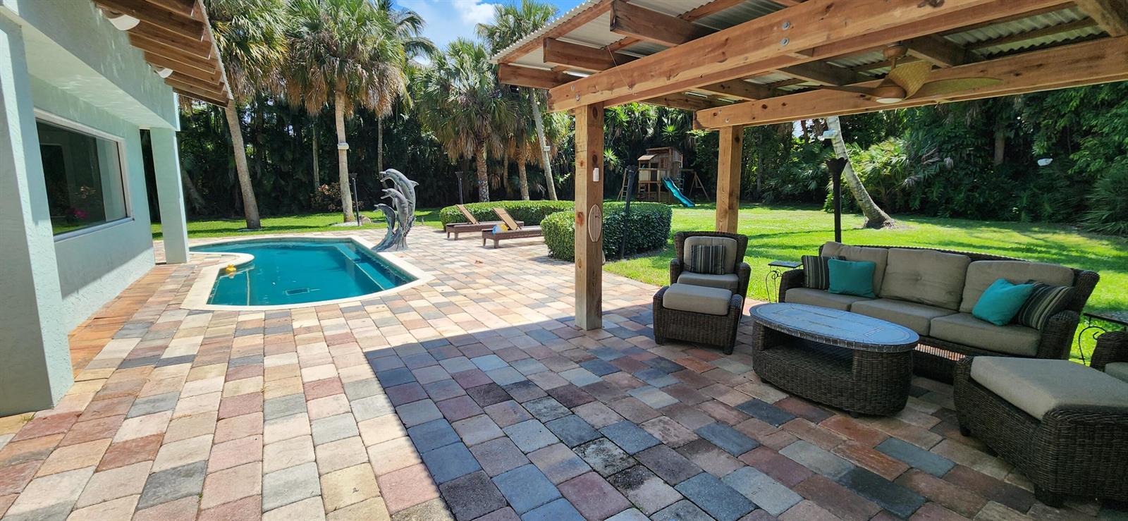 A backyard patio features a swimming pool, a covered seating area, and a grassy lawn — 1066 SE St Lucie Boulevard, Stuart FL 34996, STUART, FL