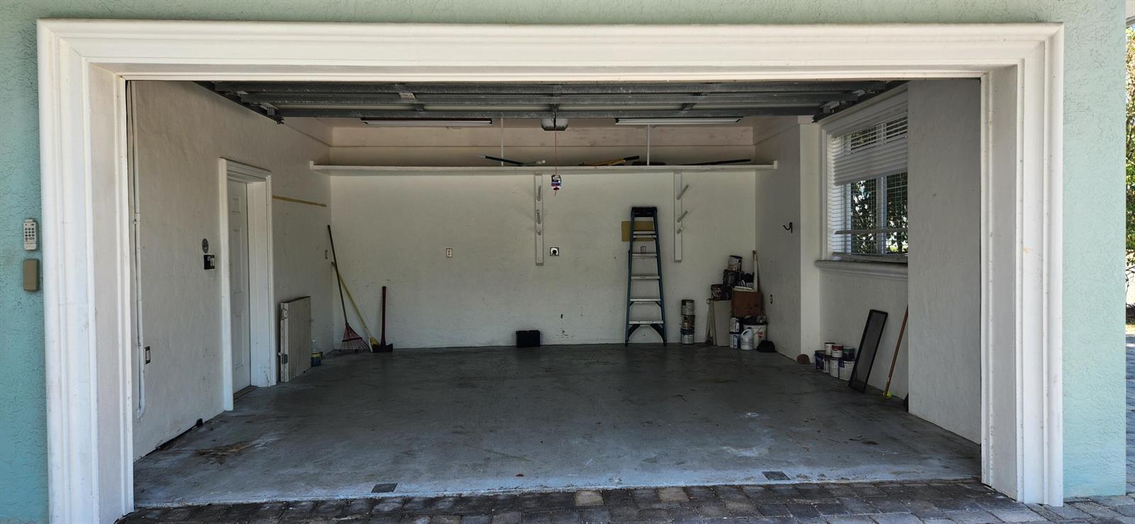 An open, empty two-car garage with white walls, a concrete floor, and a storage shelf — 1066 SE St Lucie Boulevard, Stuart FL 34996, STUART, FL