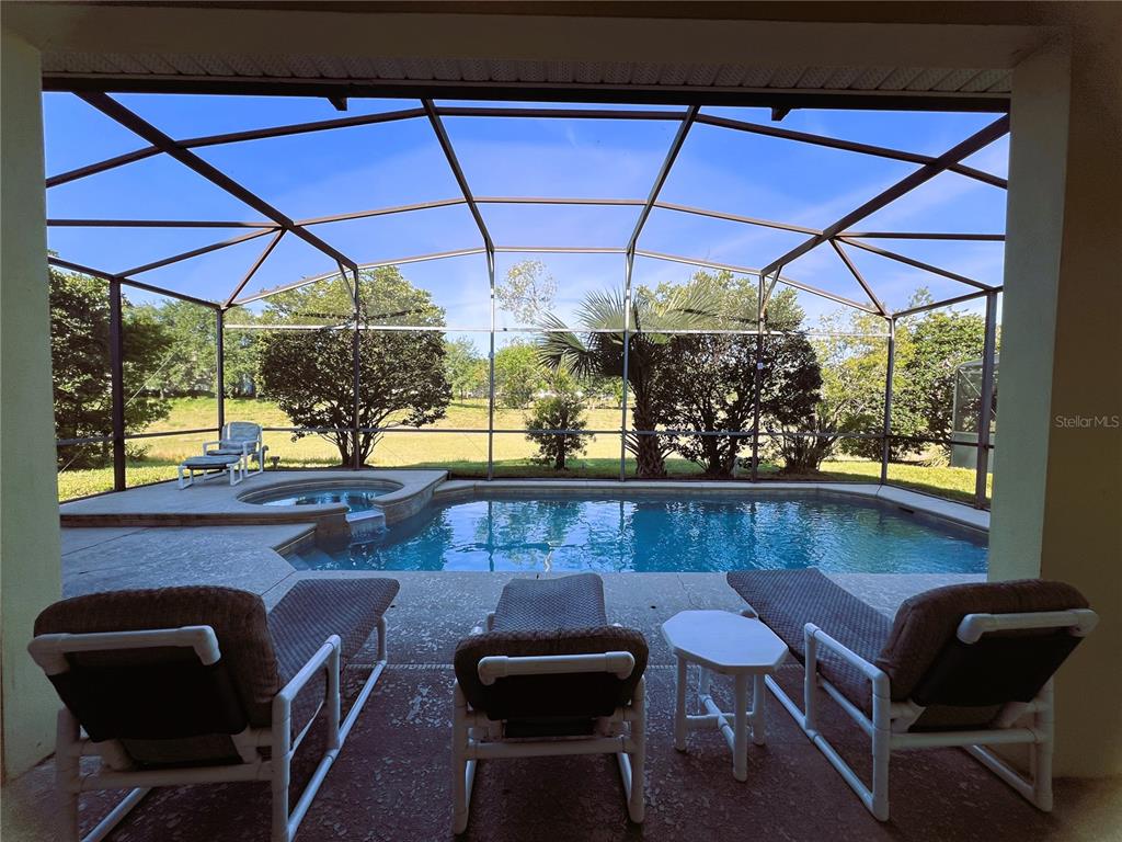 A covered patio features a swimming pool, a hot tub, and lounge chairs inside a screen enclosure — 1821 MORNING STAR DRIVE, CLERMONT, FL