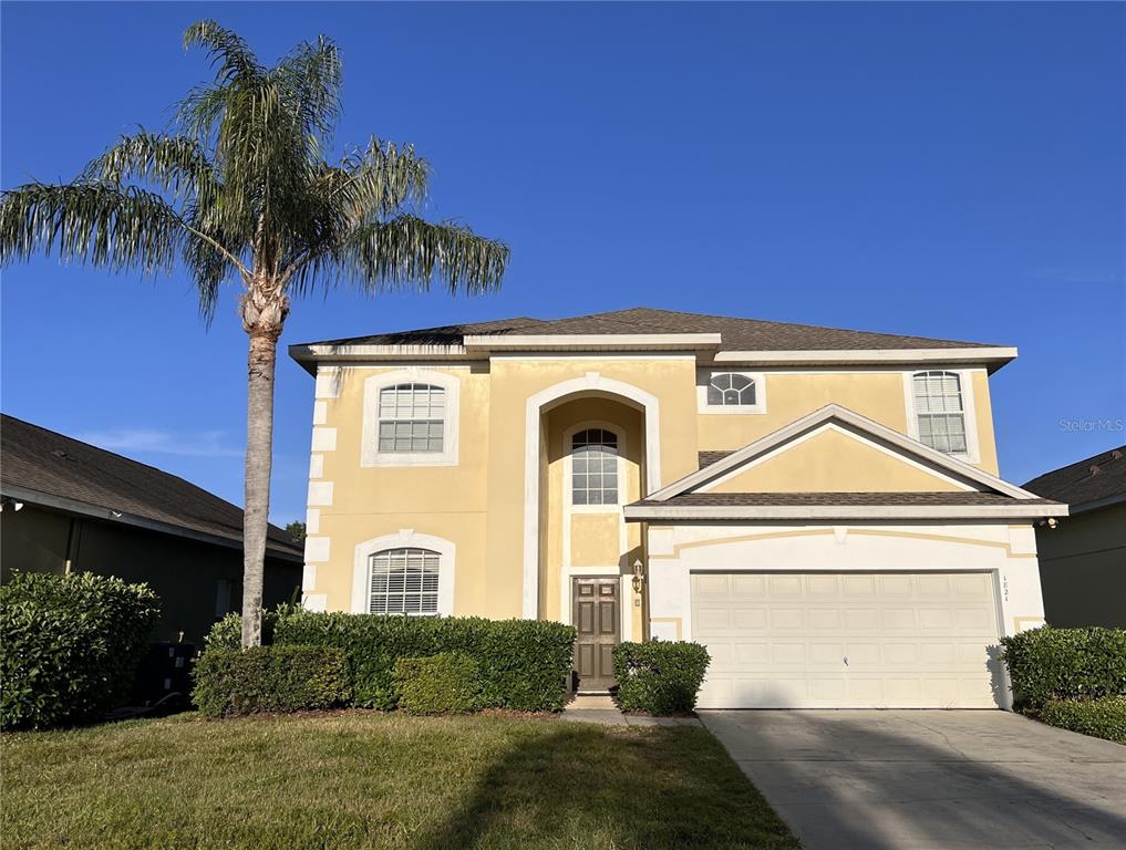 A two-story yellow stucco house features a palm tree, a front-facing garage, and arched windows — 1821 MORNING STAR DRIVE, CLERMONT, FL