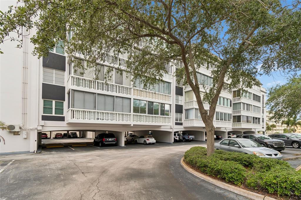 A multi-story apartment building with covered ground-level parking and mature trees in the foreground — 139 BLUFF VIEW DRIVE UNIT 110, LARGO, FL