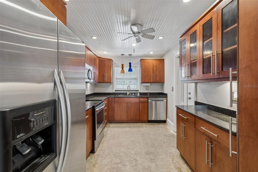 A kitchen features wood cabinets, stainless steel appliances, black countertops, and a white beadboard ceiling — 139 BLUFF VIEW DRIVE UNIT 110, LARGO, FL