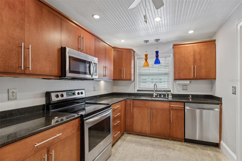 A kitchen with wood cabinets, stainless steel appliances, and black countertops under a beadboard ceiling — 139 BLUFF VIEW DRIVE UNIT 110, LARGO, FL