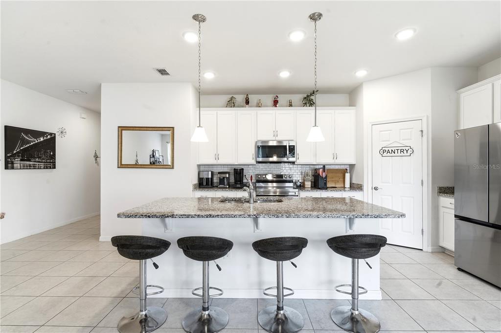 A kitchen features white cabinets, a granite-topped island with four bar stools, and stainless appliances — 24409 SUNNYS HALO WAY, SORRENTO, FL