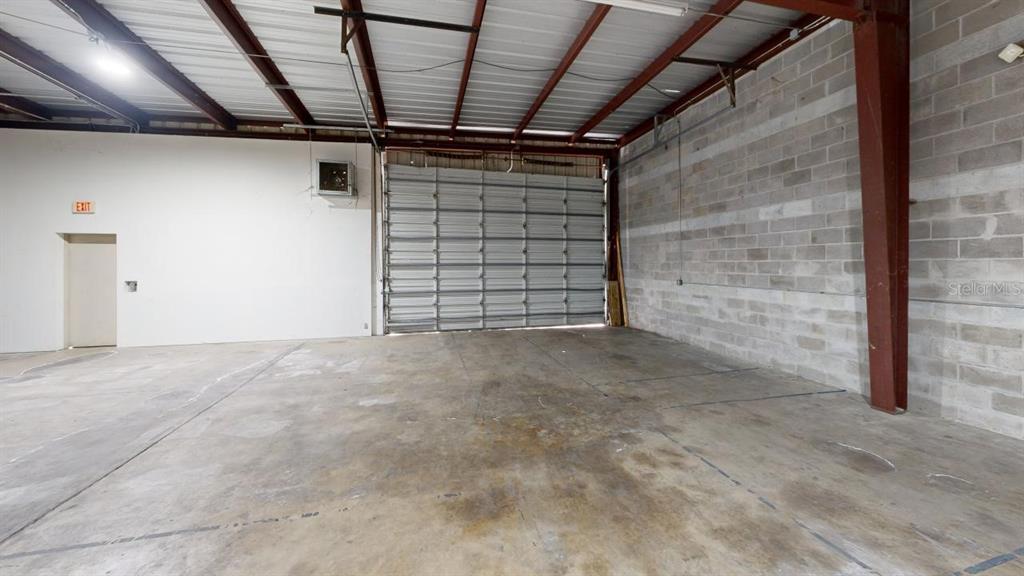 An empty warehouse space features a concrete floor, block walls, and a large roll-up door — 605 NW 53RD AVENUE UNIT A-14, GAINESVILLE, FL
