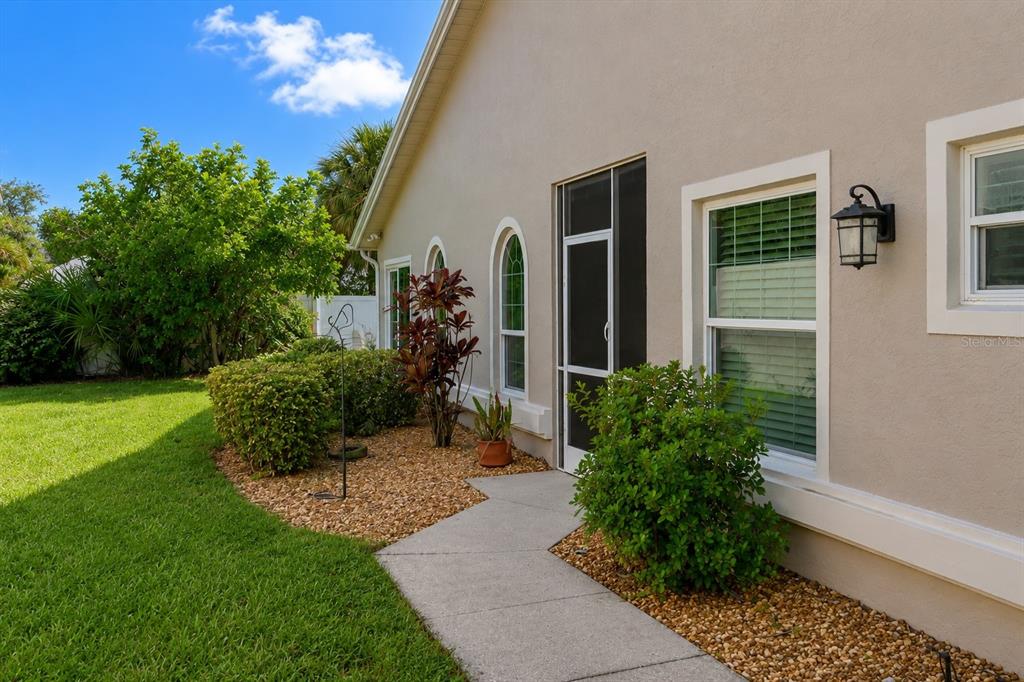 A concrete walkway leads to a screened door on the side of a beige house — 4427 MURFIELD DRIVE E, BRADENTON, FL