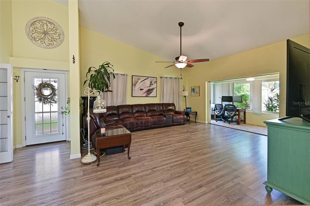 A living room features light yellow walls, wood-look flooring, a brown leather sectional, and a ceiling fan — 4427 MURFIELD DRIVE E, BRADENTON, FL