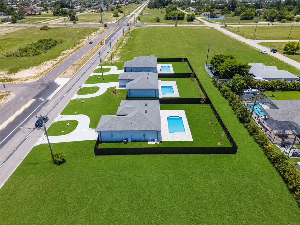 An aerial view shows three adjacent houses with private pools and fenced backyards along a road — 103 DIPLOMAT PARKWAY E, CAPE CORAL, FL