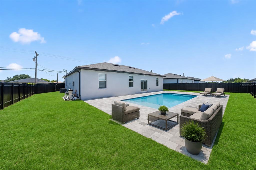 A backyard features a swimming pool, a paved patio, outdoor furniture, and a black fence — 103 DIPLOMAT PARKWAY E, CAPE CORAL, FL