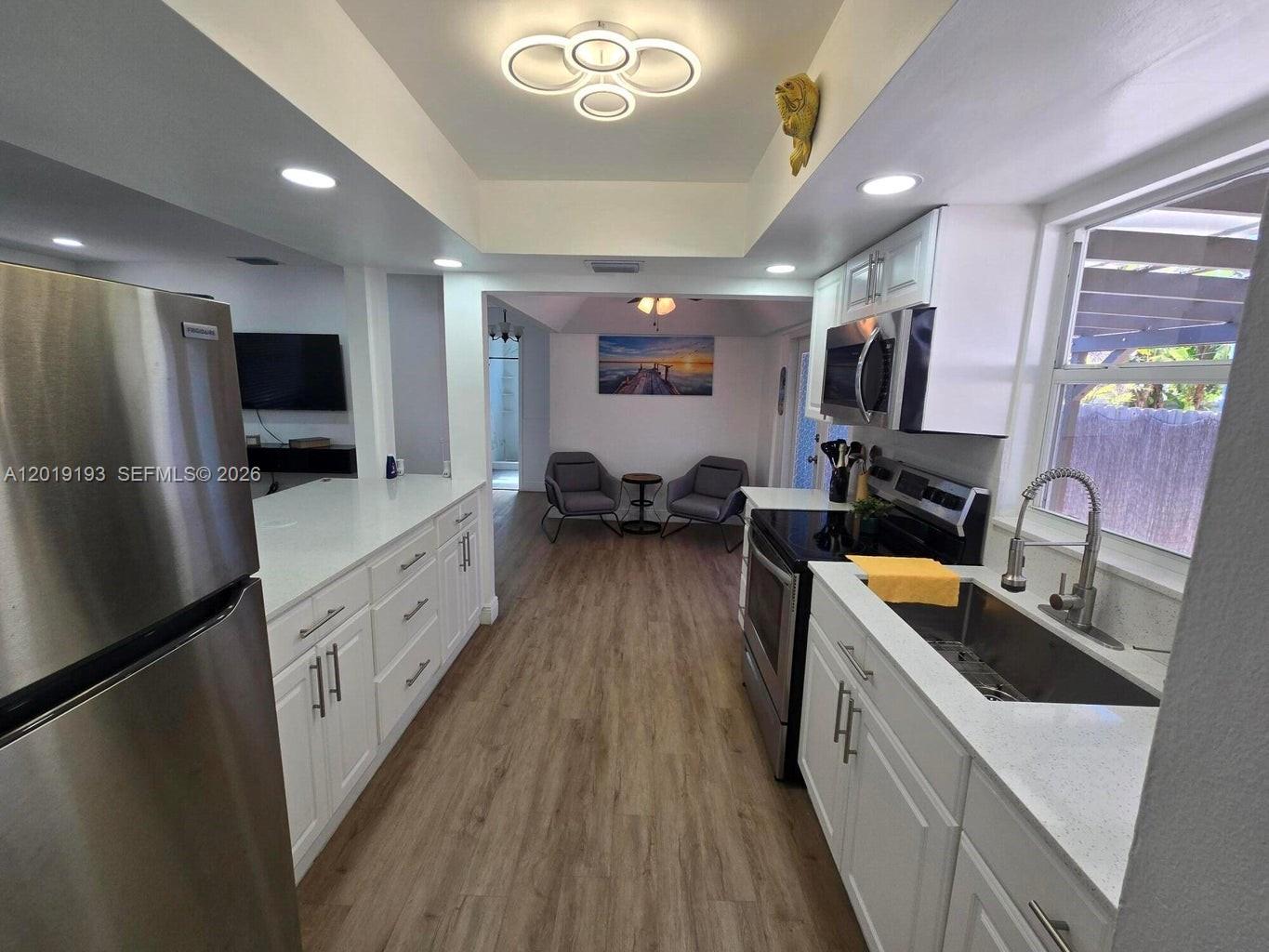 A modern kitchen with white cabinets and stainless steel appliances opens into a living area — 37 Orange Dr, Key Largo FL 33037, KEY LARGO, FL