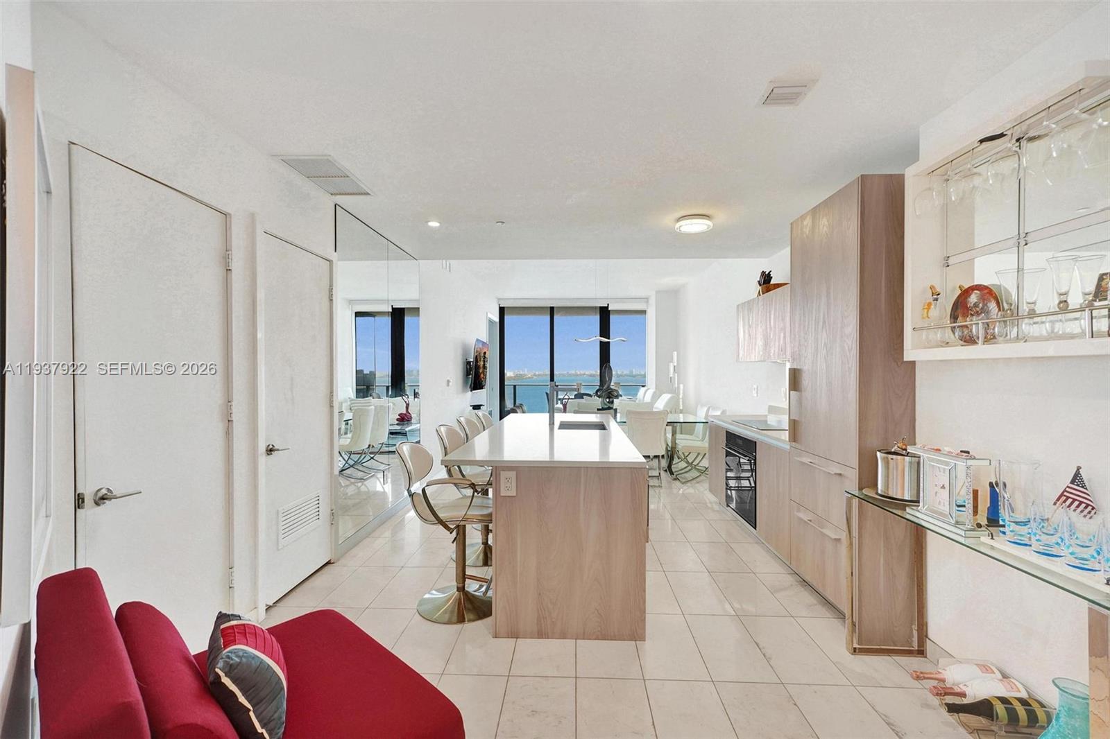 A modern kitchen with a central island and light wood cabinetry overlooks a waterfront balcony — 480 NE 31st St # 1705, Miami FL 33137, MIAMI, FL