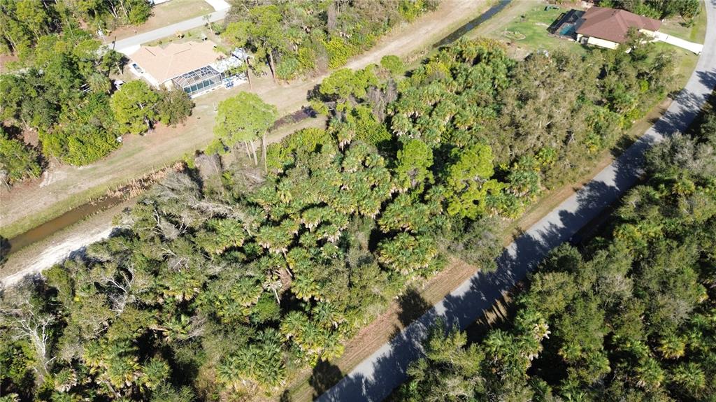 An aerial view shows a wooded, undeveloped lot situated between a paved road and canal — RAYFIELD DRIVE, NORTH PORT, FL