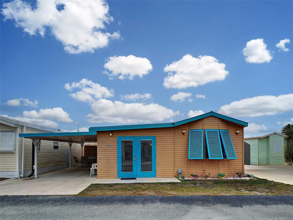 A single-story tan mobile home with blue shutters, a carport, and double glass doors — 1475 FLAMINGO DRIVE UNIT 286, ENGLEWOOD, FL